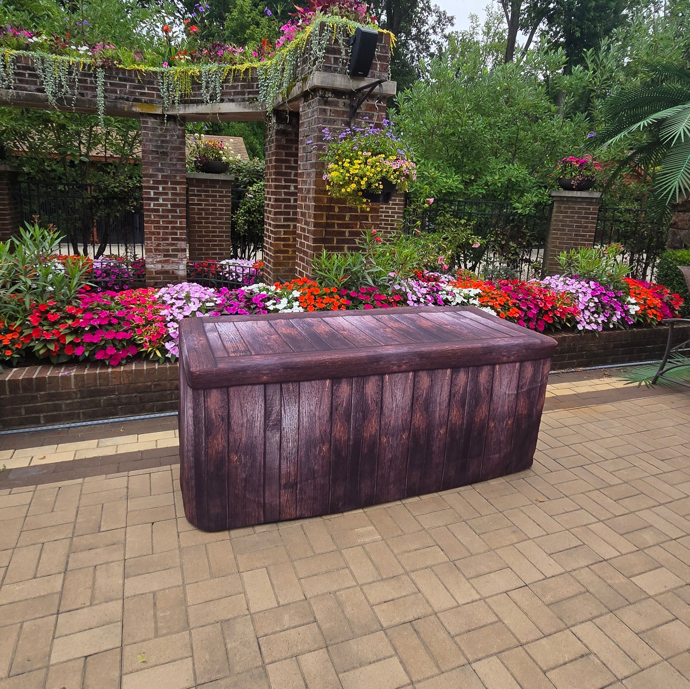A dark brown fitted table cover with a wood look outside by a pool with flowers.