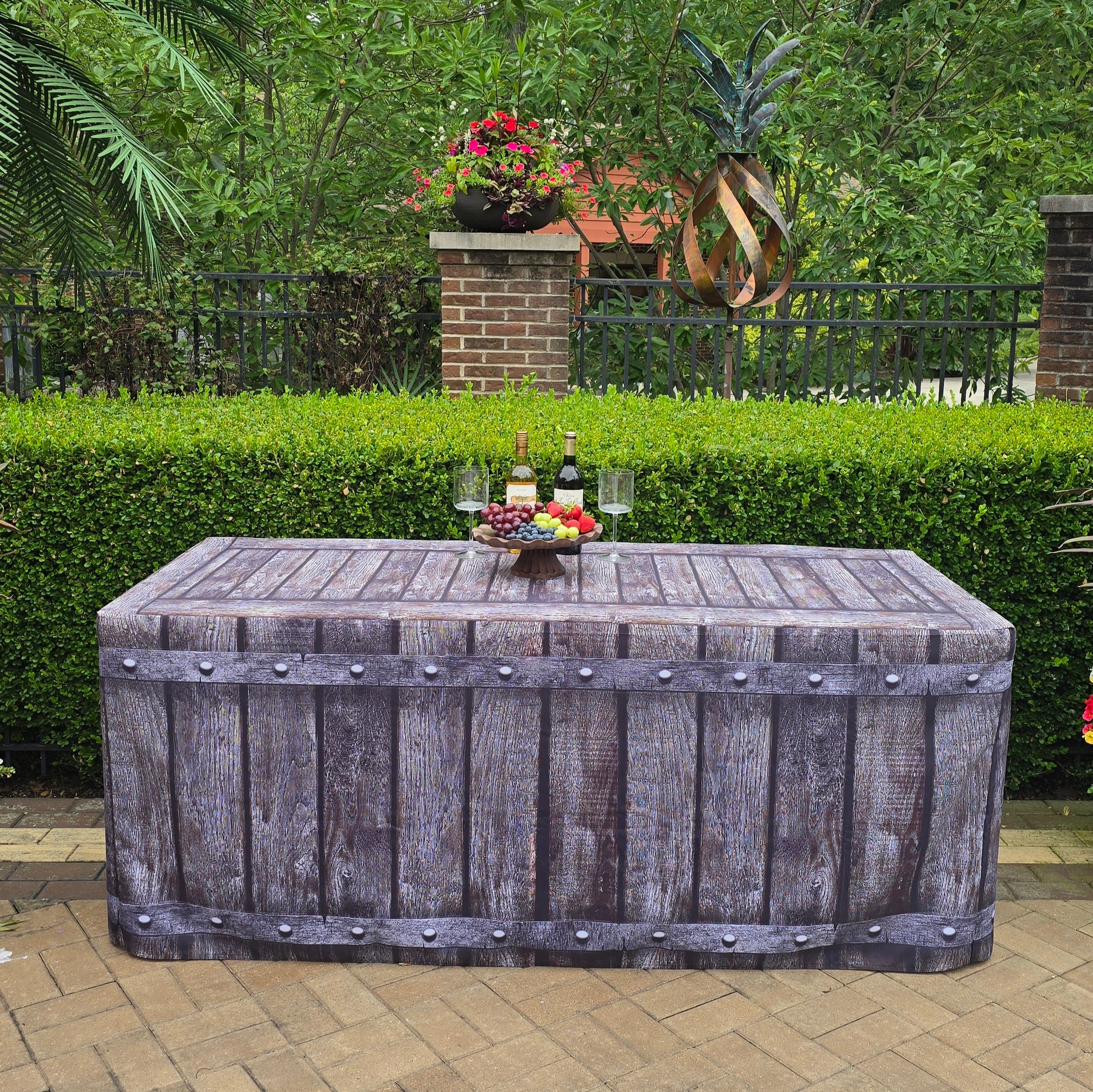 A medium size 6ft folding table covered with a gorgeous fabric fitted table cover that looks like old wood with metal rivets. Sitting outside by a pool for an outdoor event.