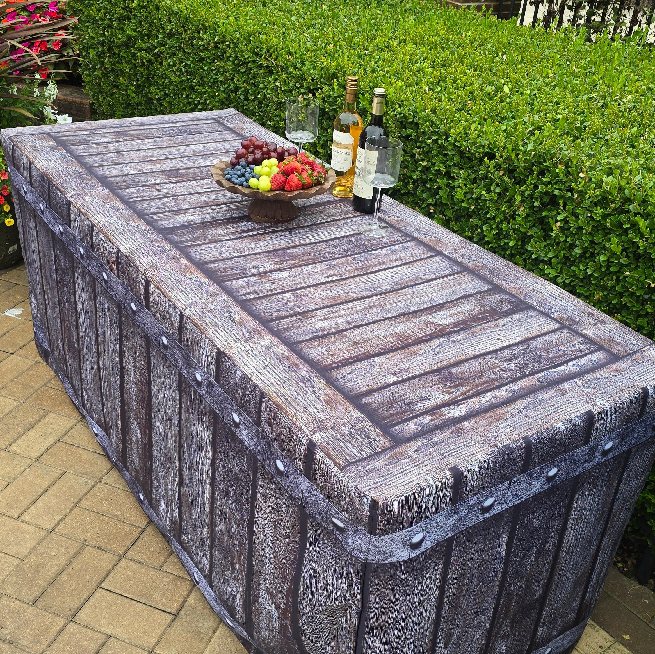 Side picture of a 6ft folding lifetime table covered with a gorgeous fitted fabric table cover that looks like real wood. On top is charcuterie food, wine and glasses for an outdoor special event.