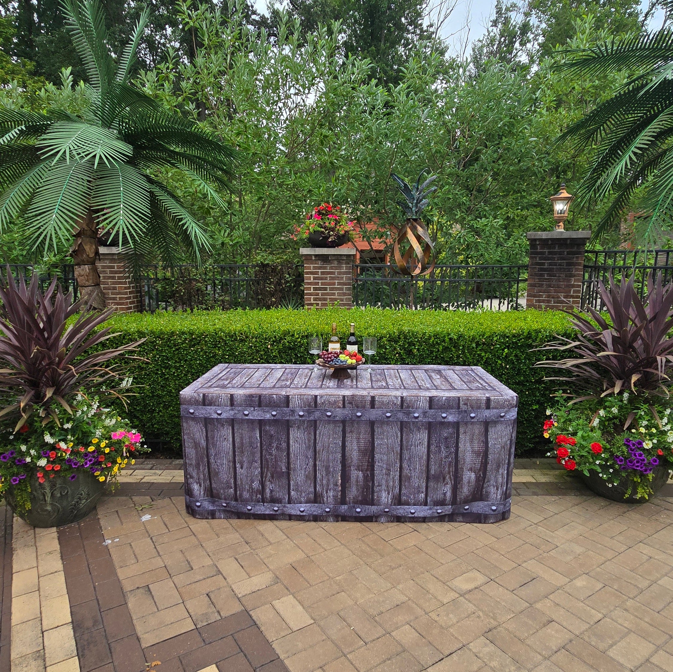 Fabric Fitted Table cover that looks like old reclaimed wood with metal rivets sitting along a row of boxwood bushes poolside at a resort.