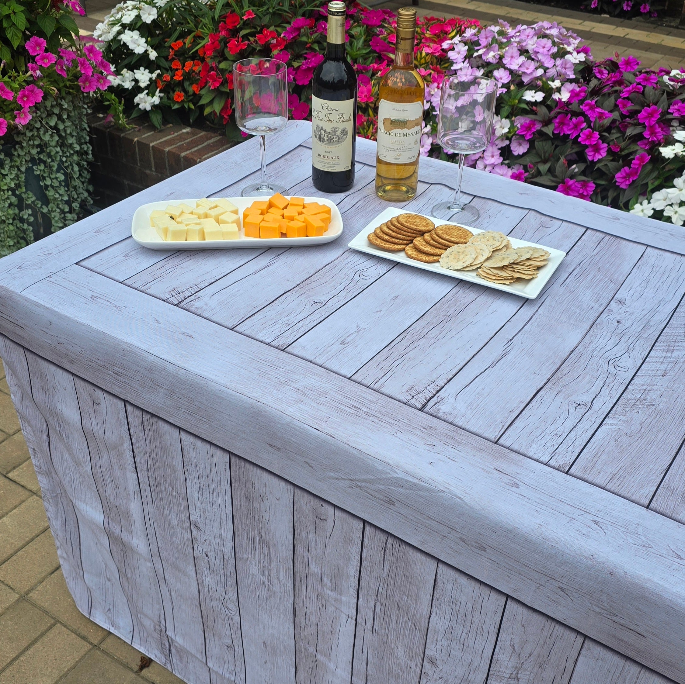 Folding table covered with a rustic white washed fabric fitted table cover that looks like wood for an outdoor casual catered event.